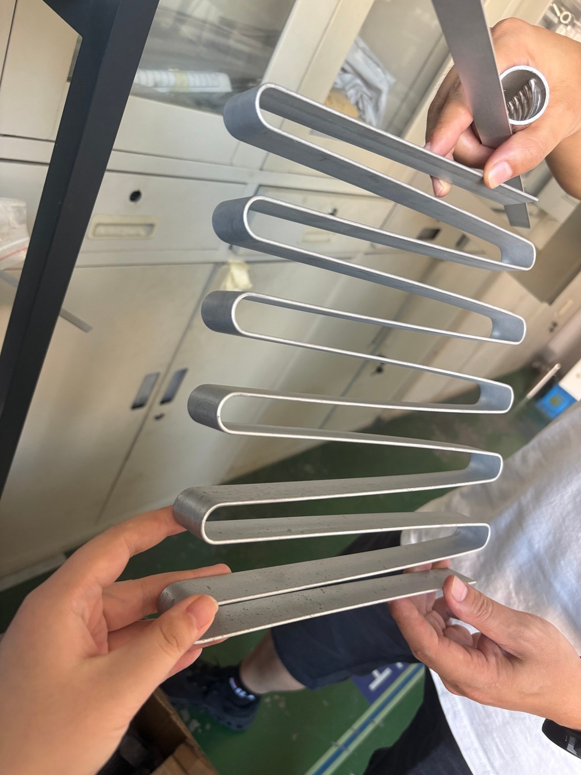 Hands holding a formed aluminium channel sample for review